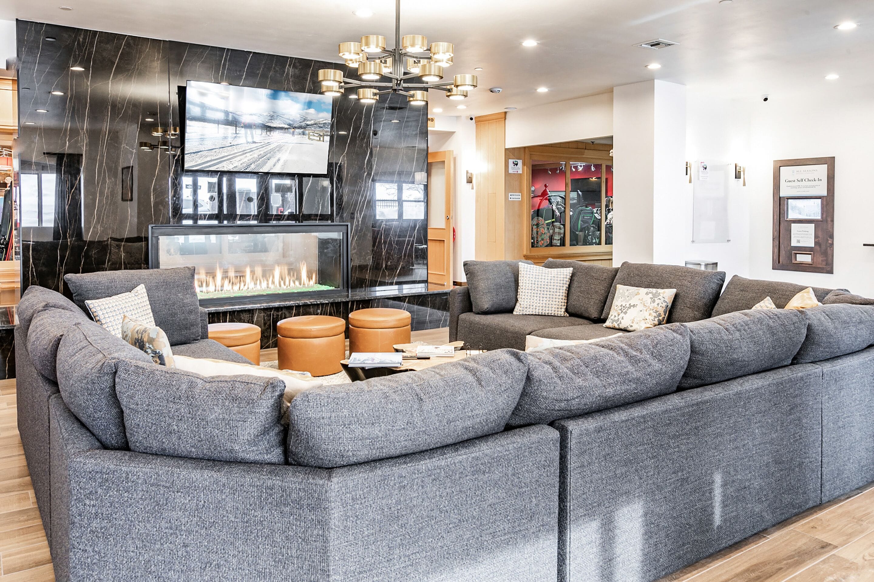 A modern living room with a large sectional sofa, a fireplace, a flat-screen TV, and a chandelier.