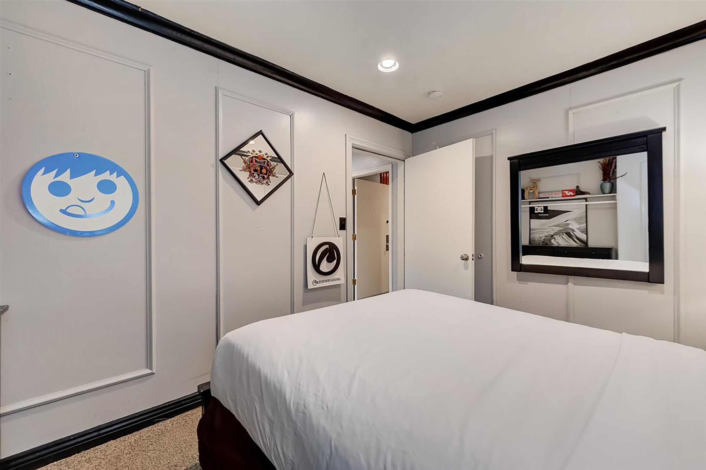 Een hotelkamer met een groot bed, een spiegel, een deur met een rond bord en een lijst met een afbeelding aan de muur.