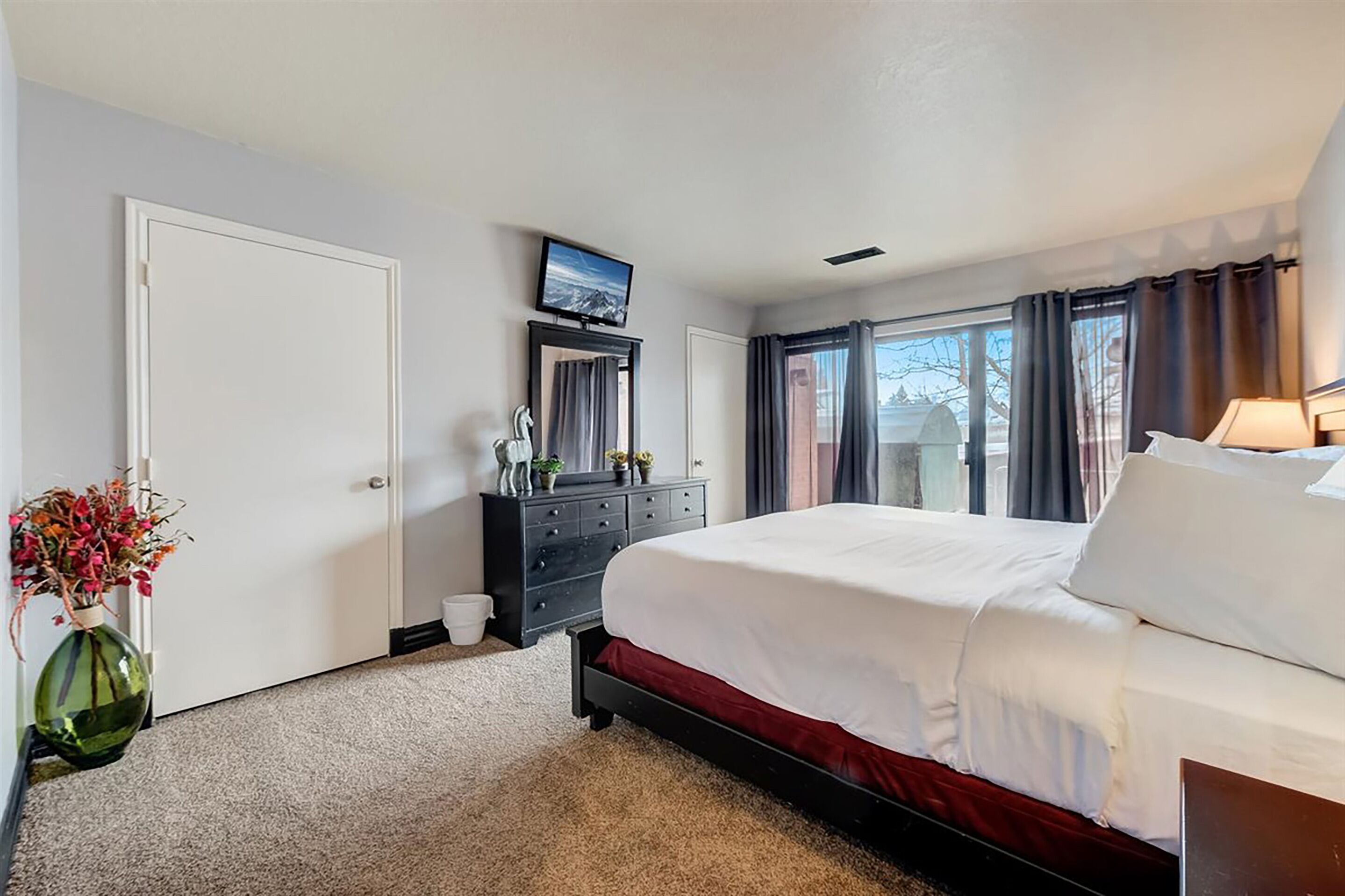 A bedroom with a large bed, a dresser, a television on a stand, and a window with curtains.