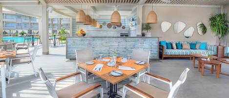 A spacious outdoor dining area with a pool view, a bar with a blue-tiled backsplash, and a seating area with striped cushions.
