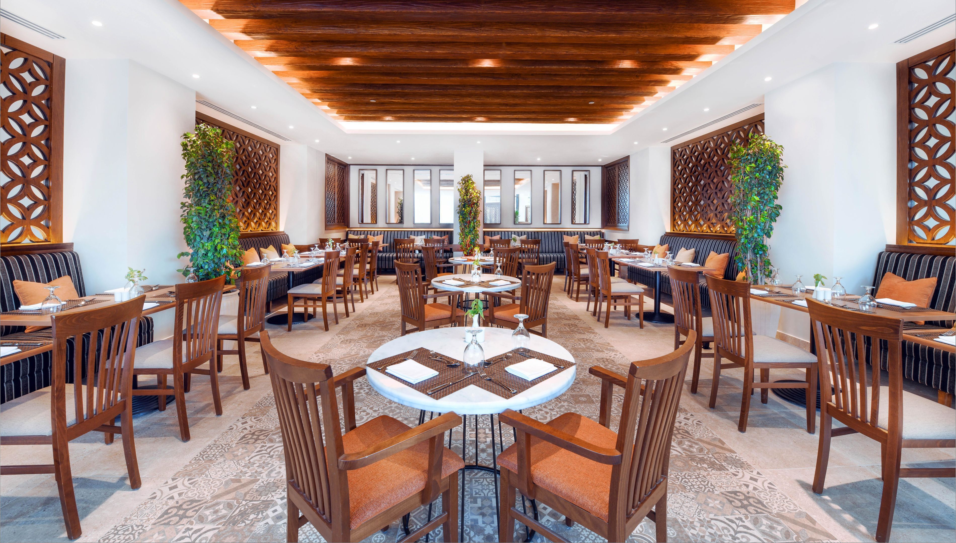 A spacious dining area with multiple round tables, wooden chairs, and a central decorative plant.