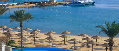 A resort with a swimming pool, beach umbrellas, and a yacht docked near the water.