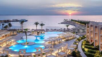 Ein Resort mit einem großen Pool, Liegestühlen und Blick auf das Meer bei Sonnenuntergang.