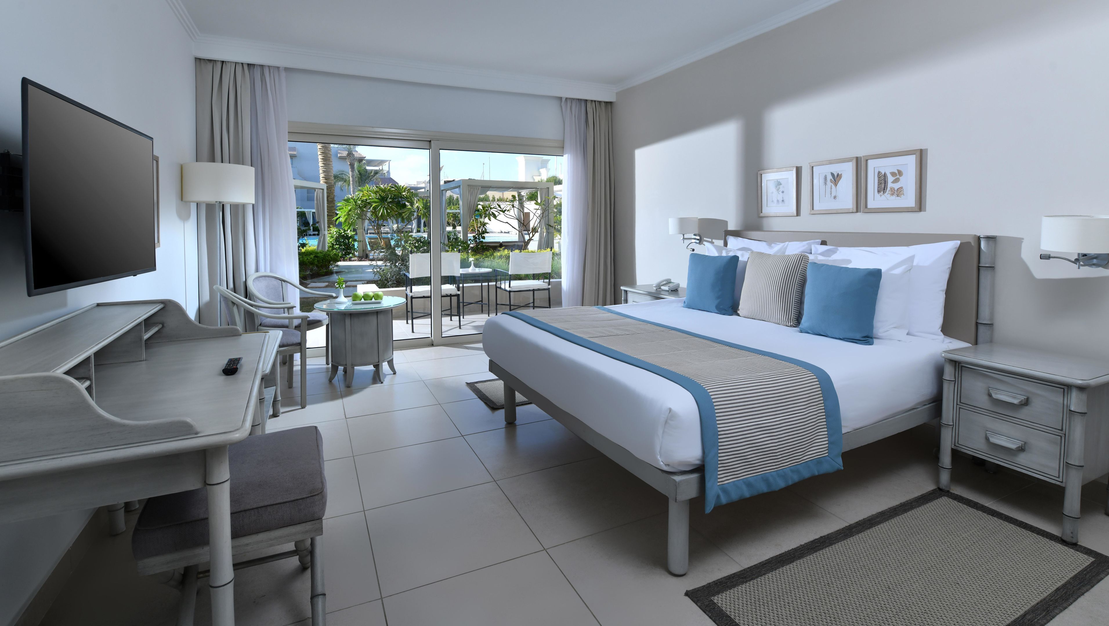 Ein Hotelzimmer mit Bett, Schreibtisch, Stuhl, Fernseher und einem Balkon mit Sitzgelegenheit.