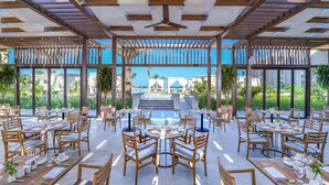 An outdoor dining area with multiple tables and chairs, a pool in the background, and a view of a resort complex. - JAZ Elite Casa Del Mar Beach - All inclusive (Hurghada)