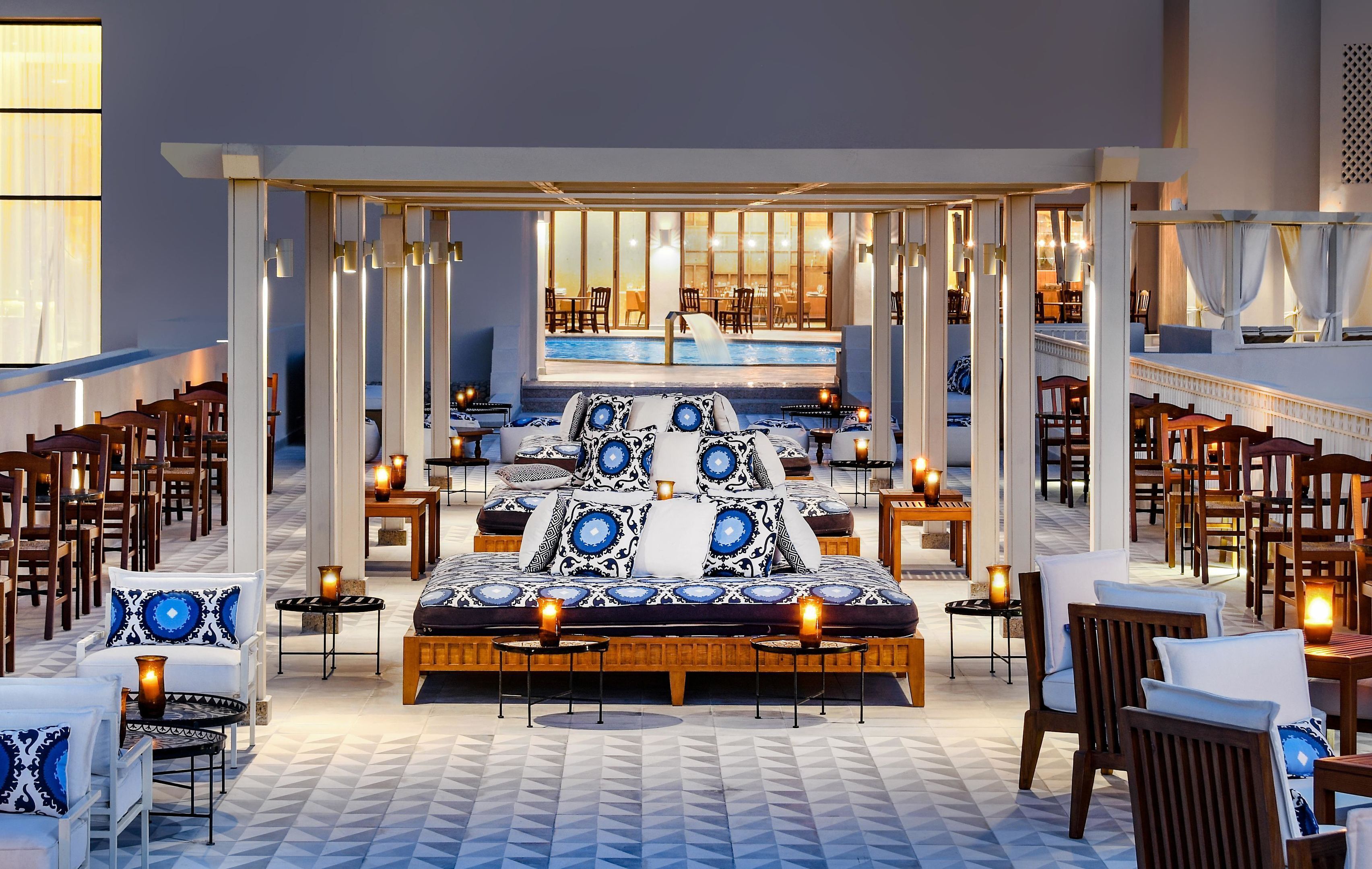 A hotel lobby with a central seating area, a pool, and multiple dining tables.