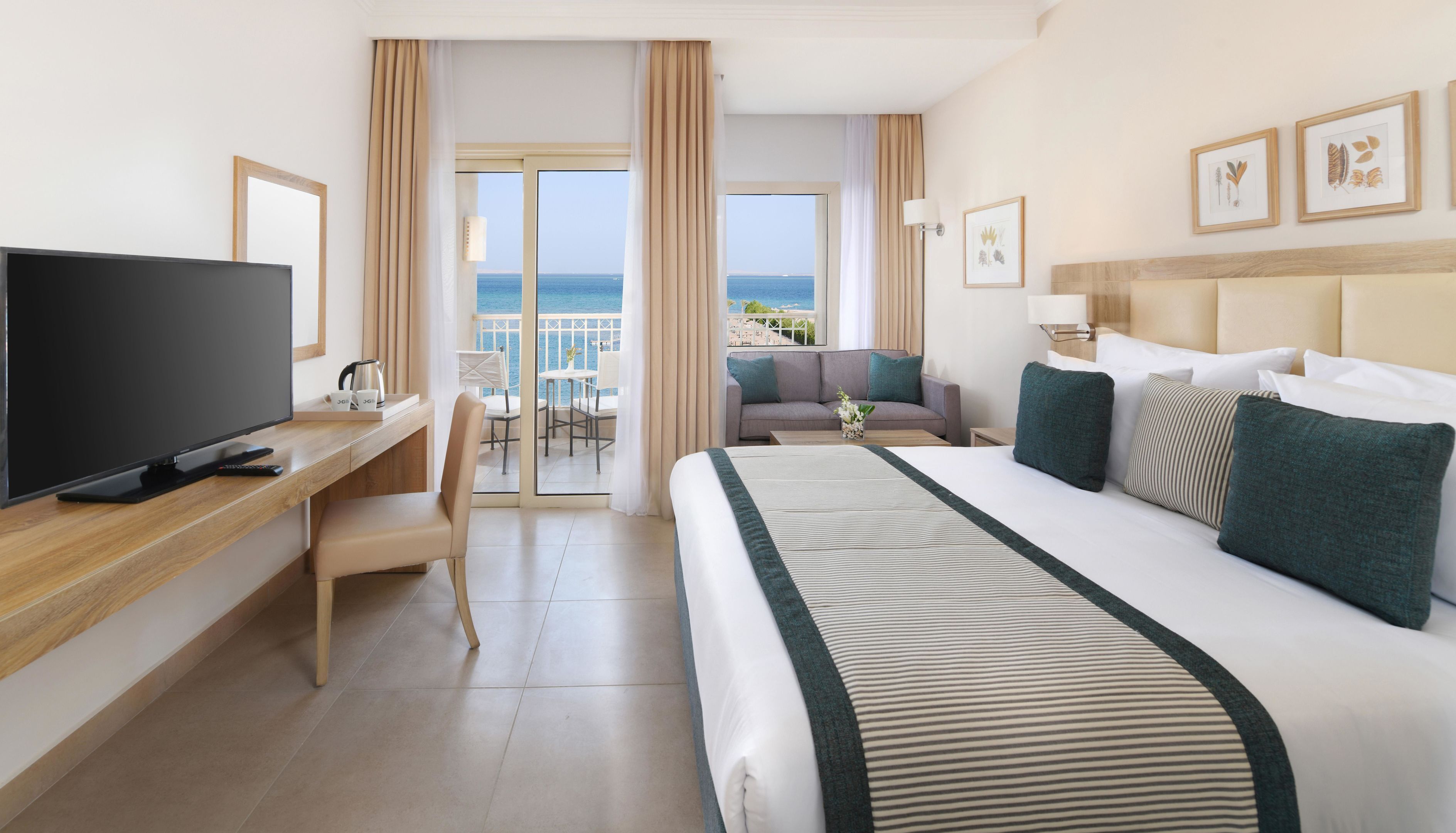 Habitación de hotel con cama, televisión, escritorio, silla, sofá y balcón con vista al mar.
