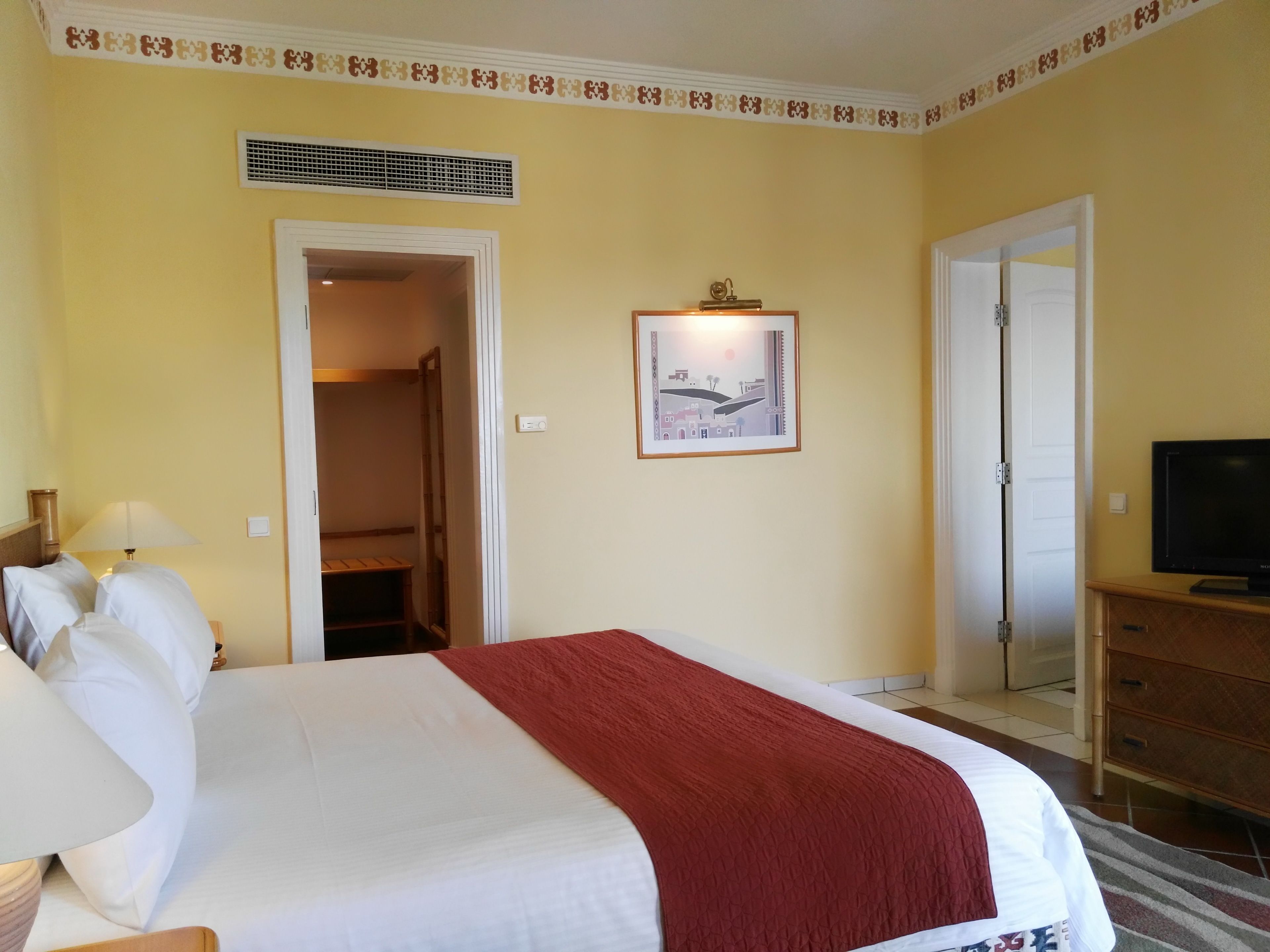Ein Hotelzimmer mit Bett, Fernseher, Tür und einem gerahmten Bild an der Wand.