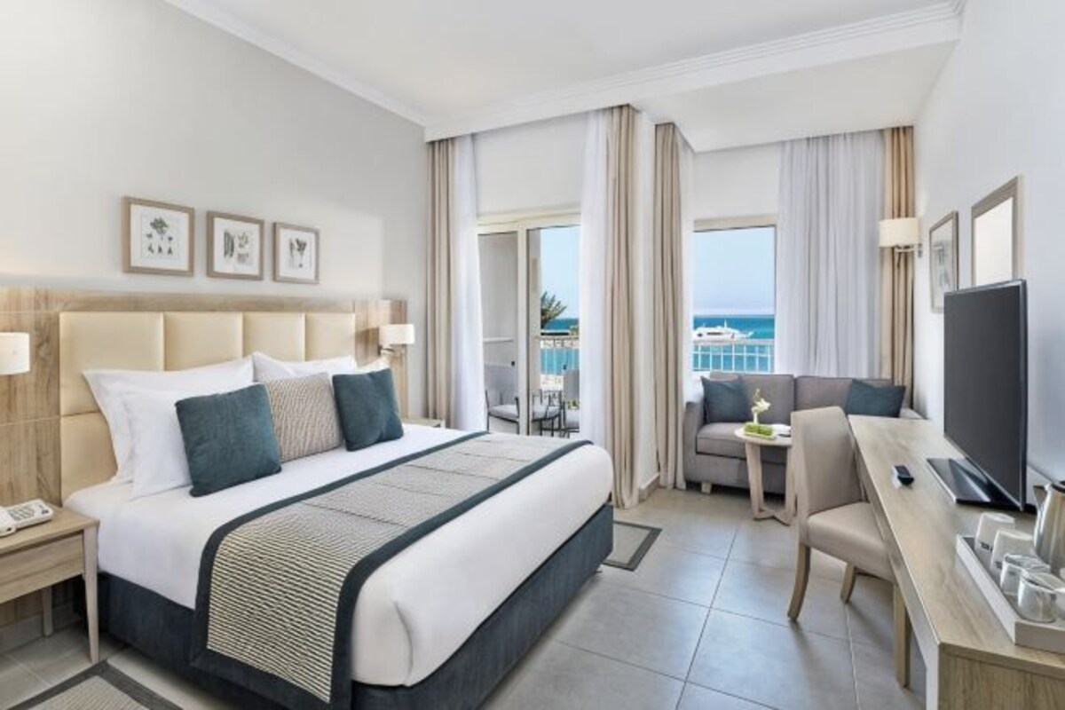 A hotel room with a large bed, a desk, a chair, a TV, and a balcony with a view.