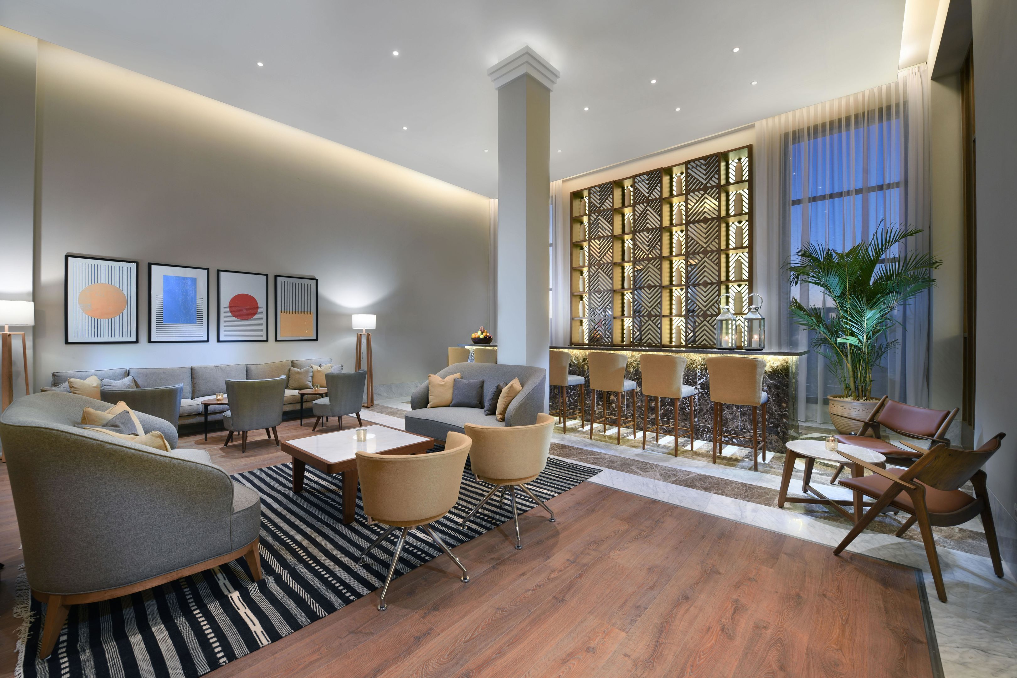 A modern hotel lobby with a seating area, a bar, and a decorative wall.