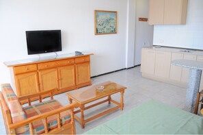 A living room with a sofa, a coffee table, a TV, wooden cabinets, and a kitchen area with a countertop and cabinets. - Apartamentos Roque Nublo (San Bartolomé de Tirajana)