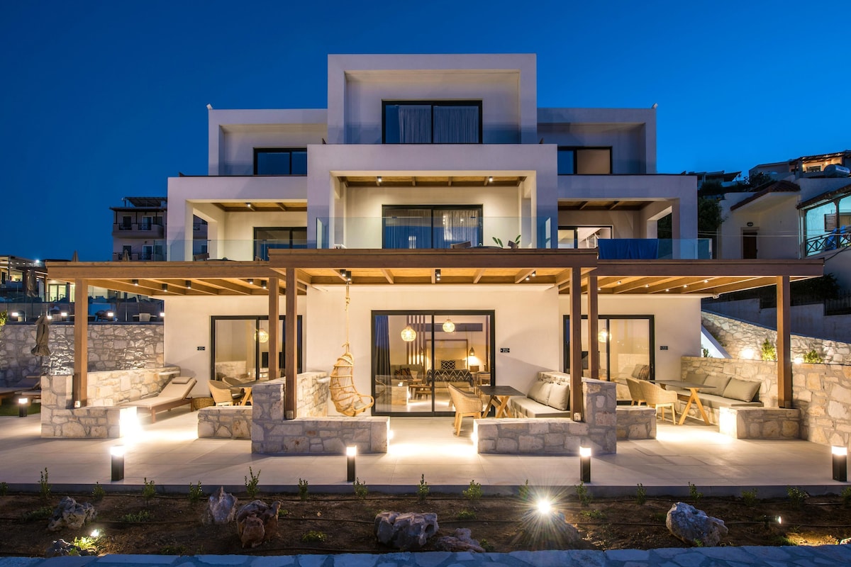 A modern multi-story building with a covered outdoor seating area featuring stone walls and wooden furniture.