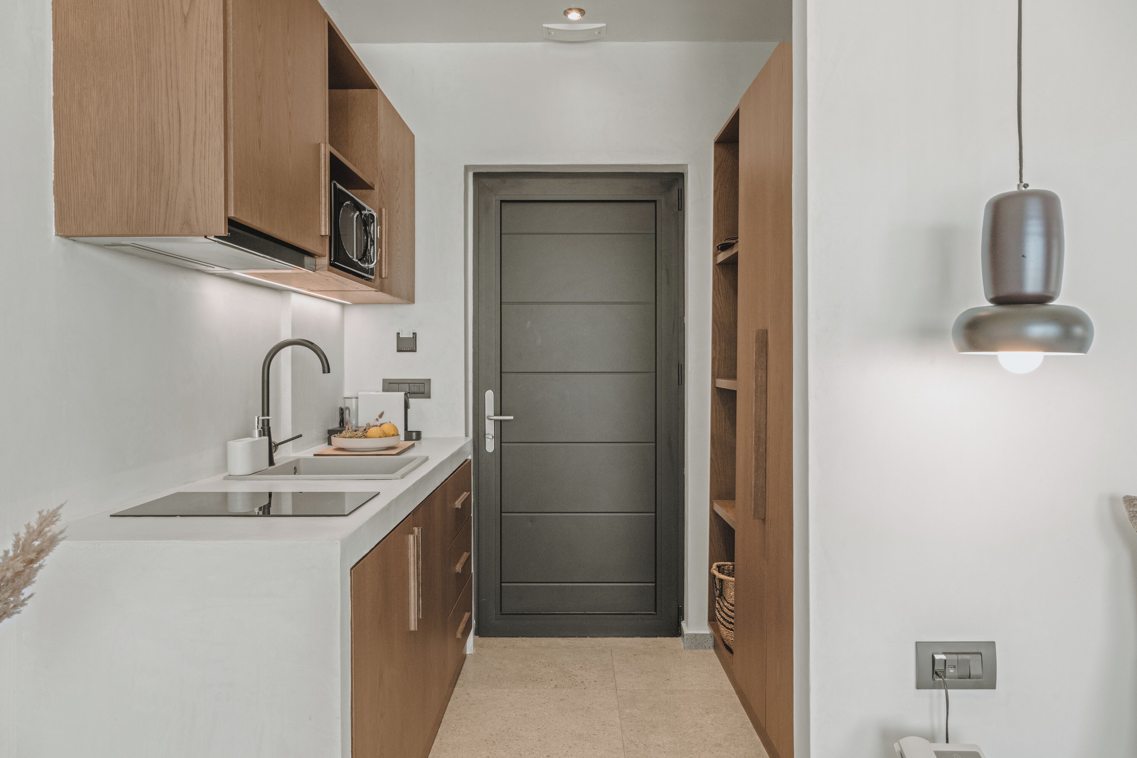A modern kitchen with a white countertop, wooden cabinets, and a dark door.