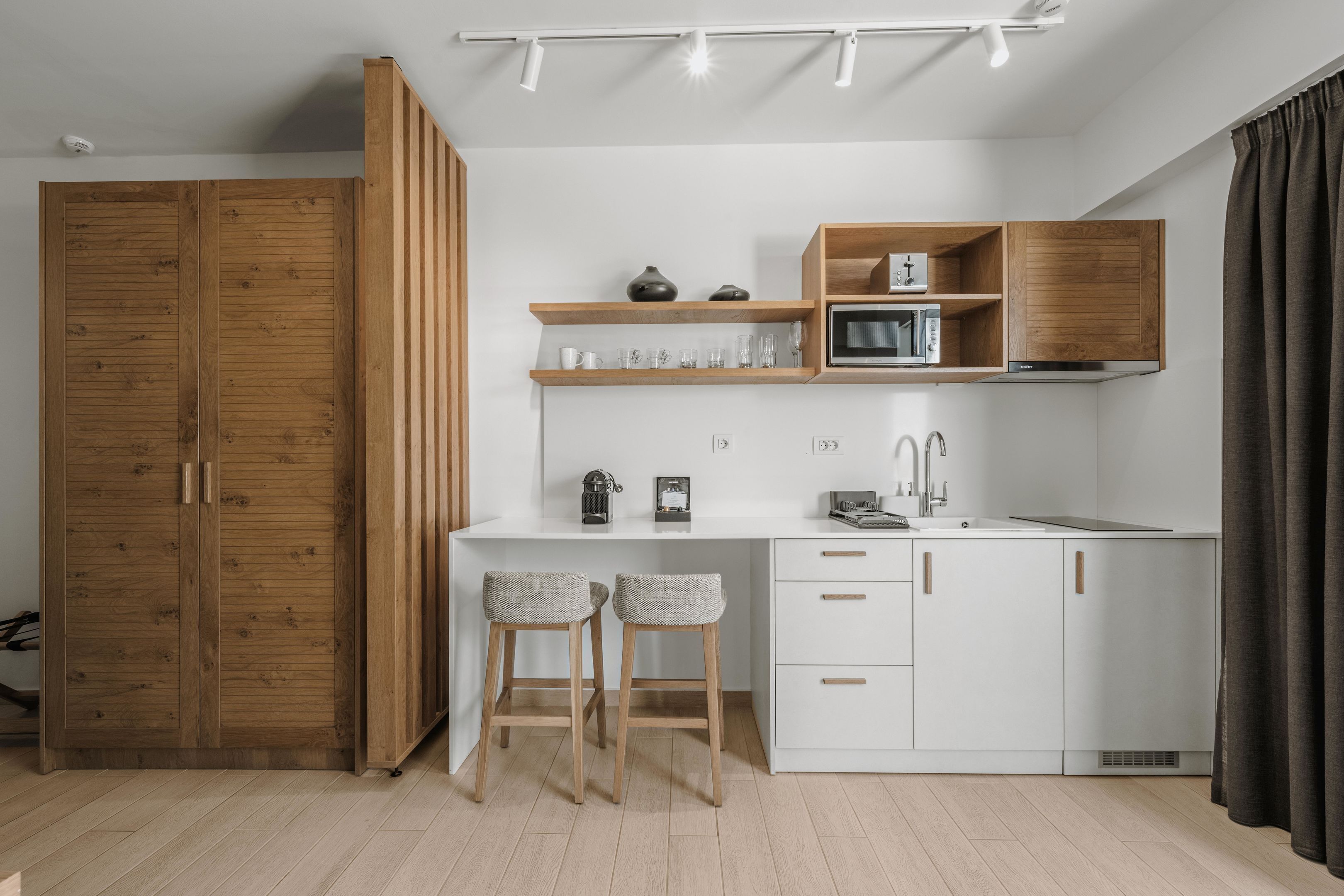 A modern kitchen with white cabinets, wooden shelves, and two bar stools.
