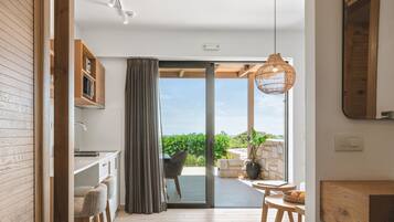 Een moderne keuken met houten kastjes, een eethoek met tafel en stoelen, en een schuifdeur naar een terras met uitzicht op groen.