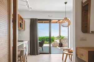Una cocina moderna con armarios de madera, un comedor con mesa y sillas, y un amplio ventanal corredizo que da a un patio exterior con vistas a zonas verdes.