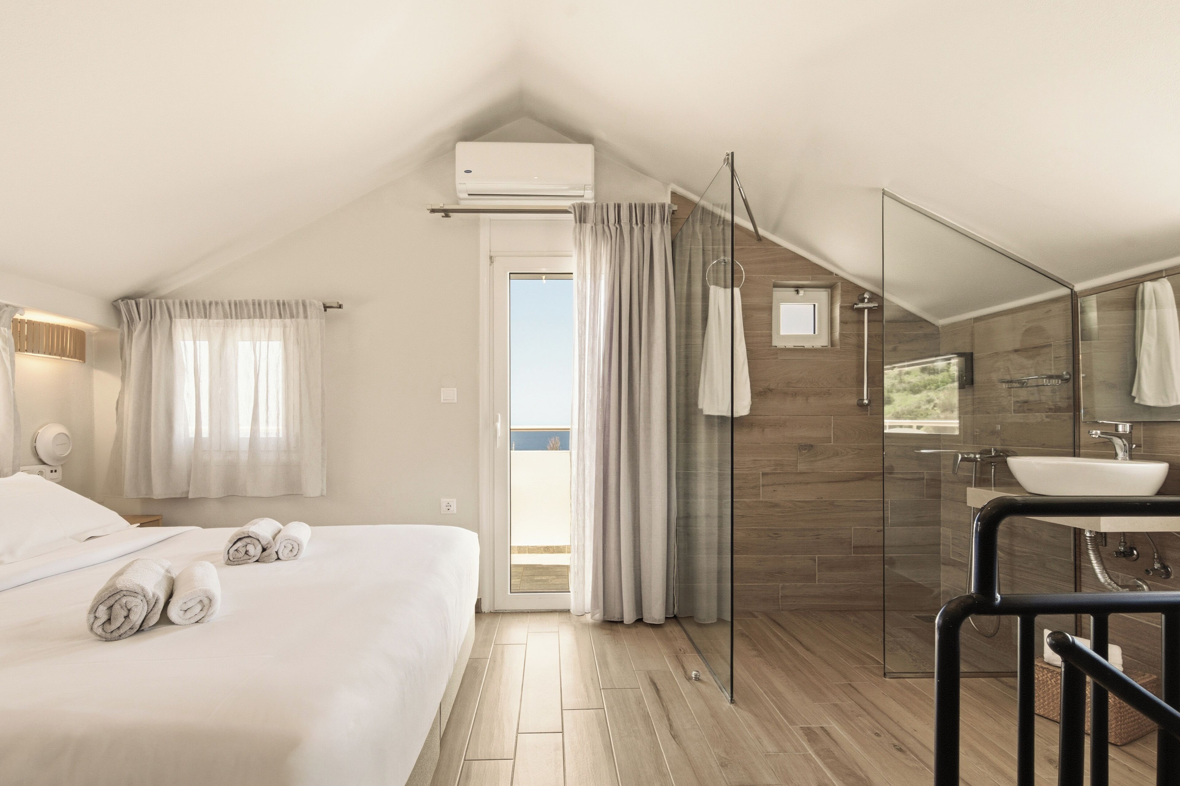 A modern hotel room with a bed, a bathroom with a sink and mirror, and a view of the outdoors.