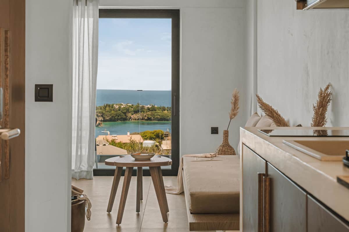 A modern kitchen with a view of the sea, a dining area with a table and chairs, and a sofa.