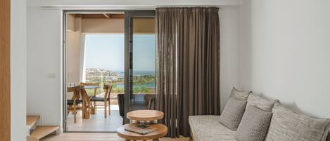A modern living room with a sofa, a small round table with a book, and a view of the outdoors through a glass door.
