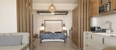 A compact room with a bed, a sofa, a kitchenette, and a ceiling fan.
