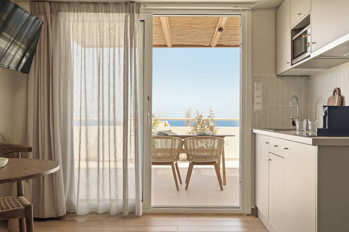 A kitchen with a view to the sea, a dining area with chairs, and a table.
