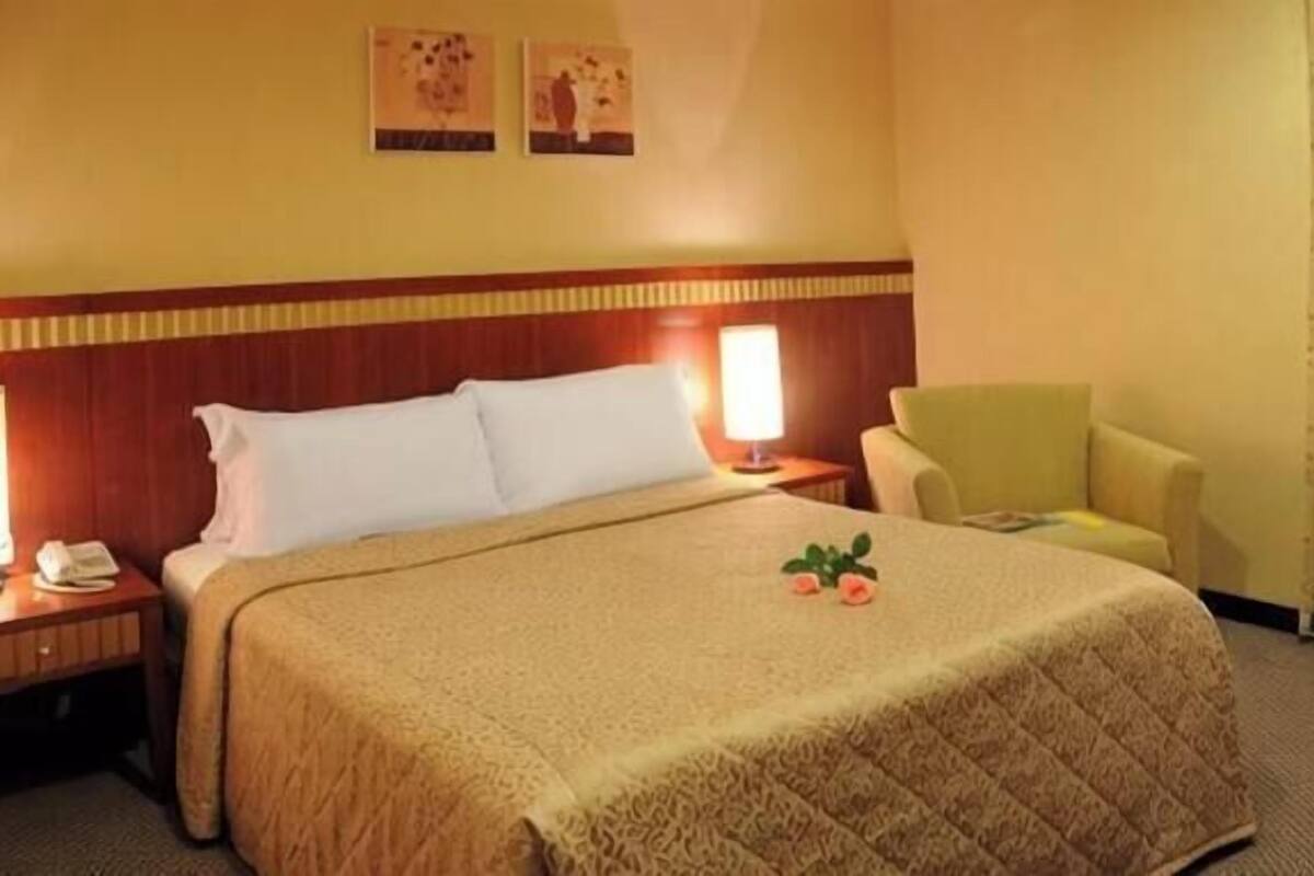 A hotel room with a bed, bedside lamps, a chair, and a small table with a phone.