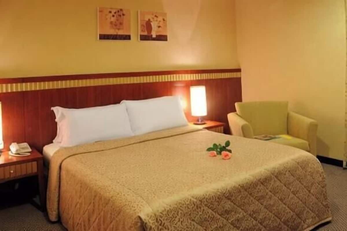 A hotel room with a bed, bedside lamps, a chair, and a small table with a phone.