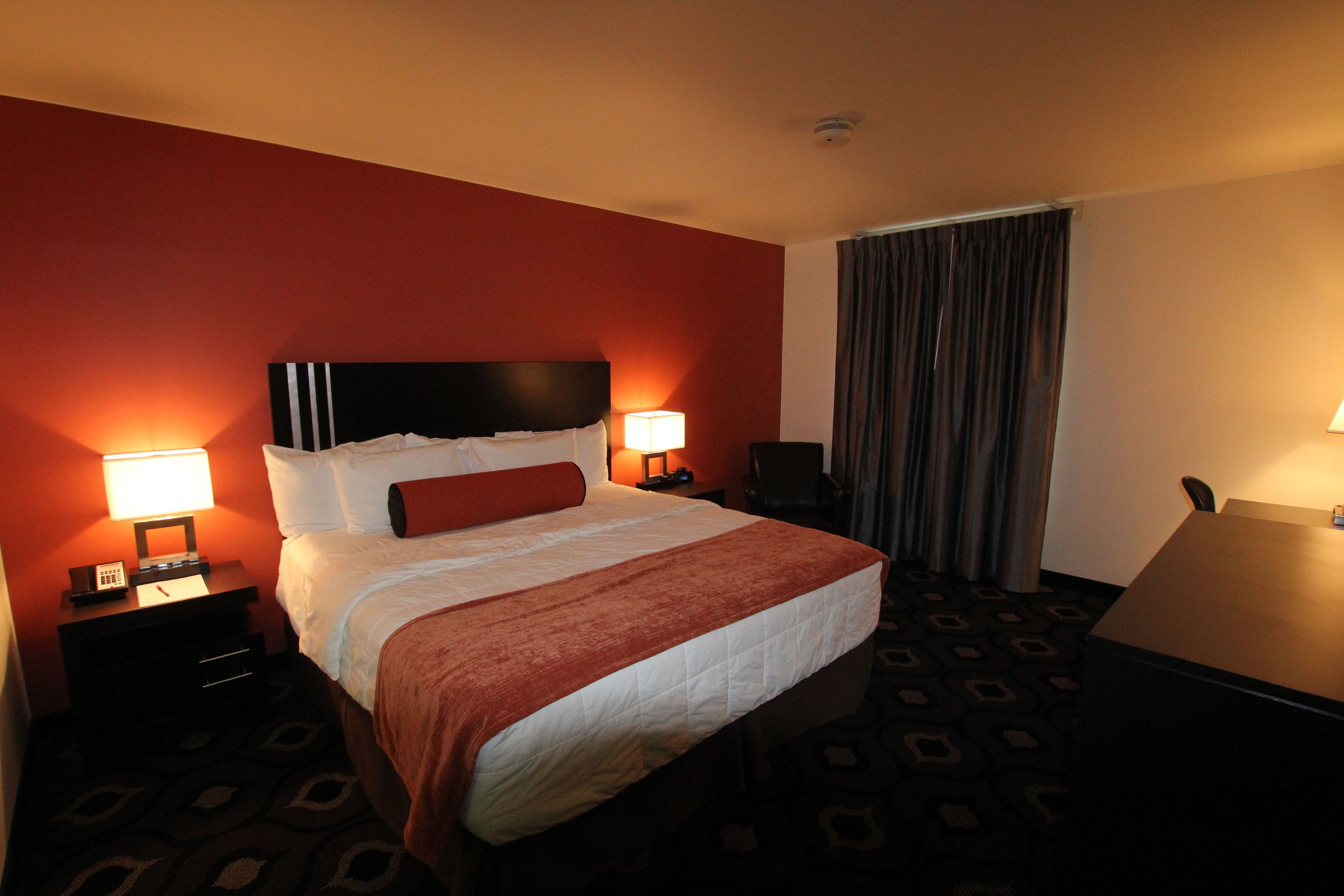 Habitación de hotel con una cama grande, dos mesitas de noche con lámparas, un escritorio y una ventana con cortinas.