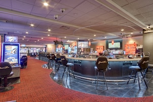 Zona de bar en un casino con varias máquinas tragamonedas, una barra y varios taburetes.