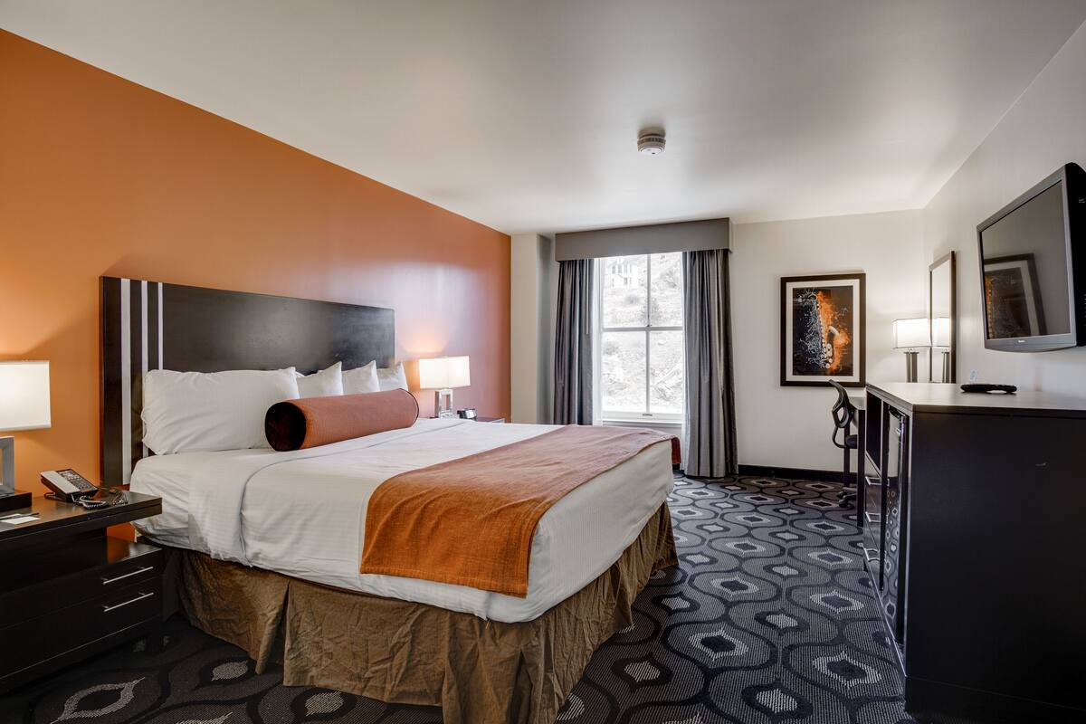 A hotel room with a large bed, a desk with a lamp, a TV, and a window with curtains.
