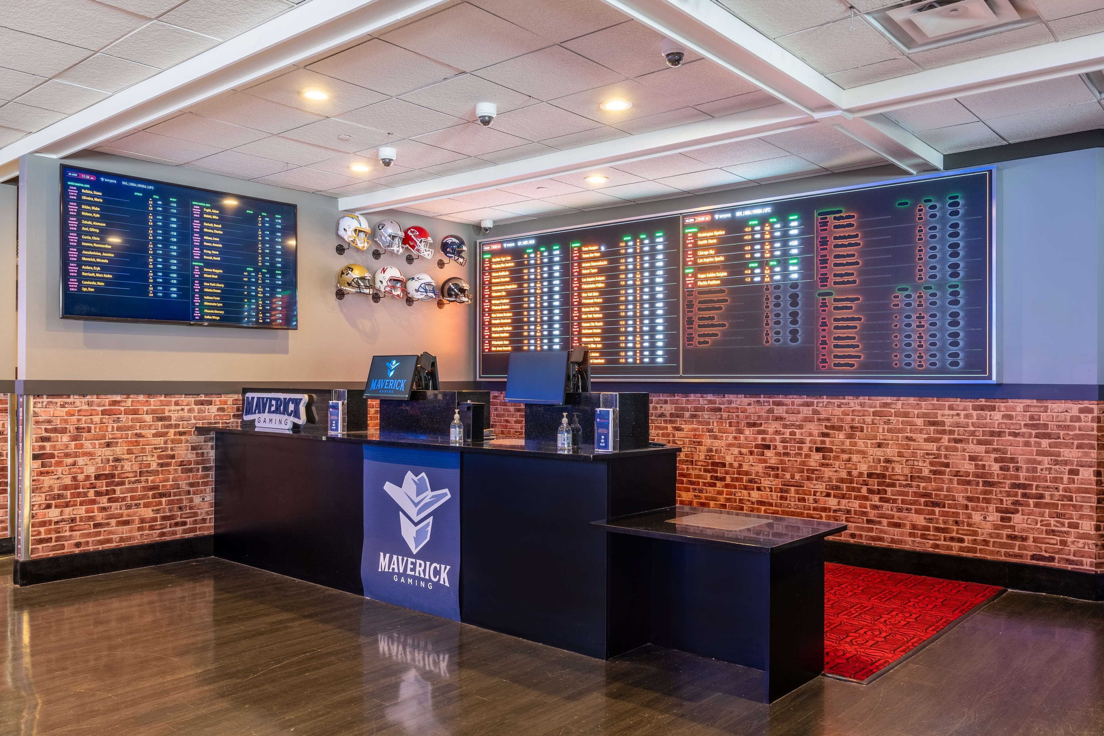 A gaming lobby with a brick wall, a digital scoreboard, and a Maverick Gaming sign.