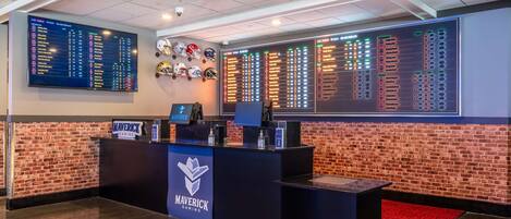 A gaming lobby with a brick wall, a digital scoreboard, and a Maverick Gaming sign.