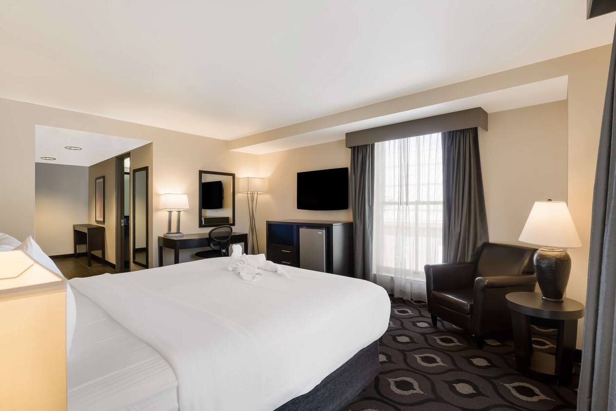A hotel room with a large bed, a desk, a chair, a TV, and a window with curtains.