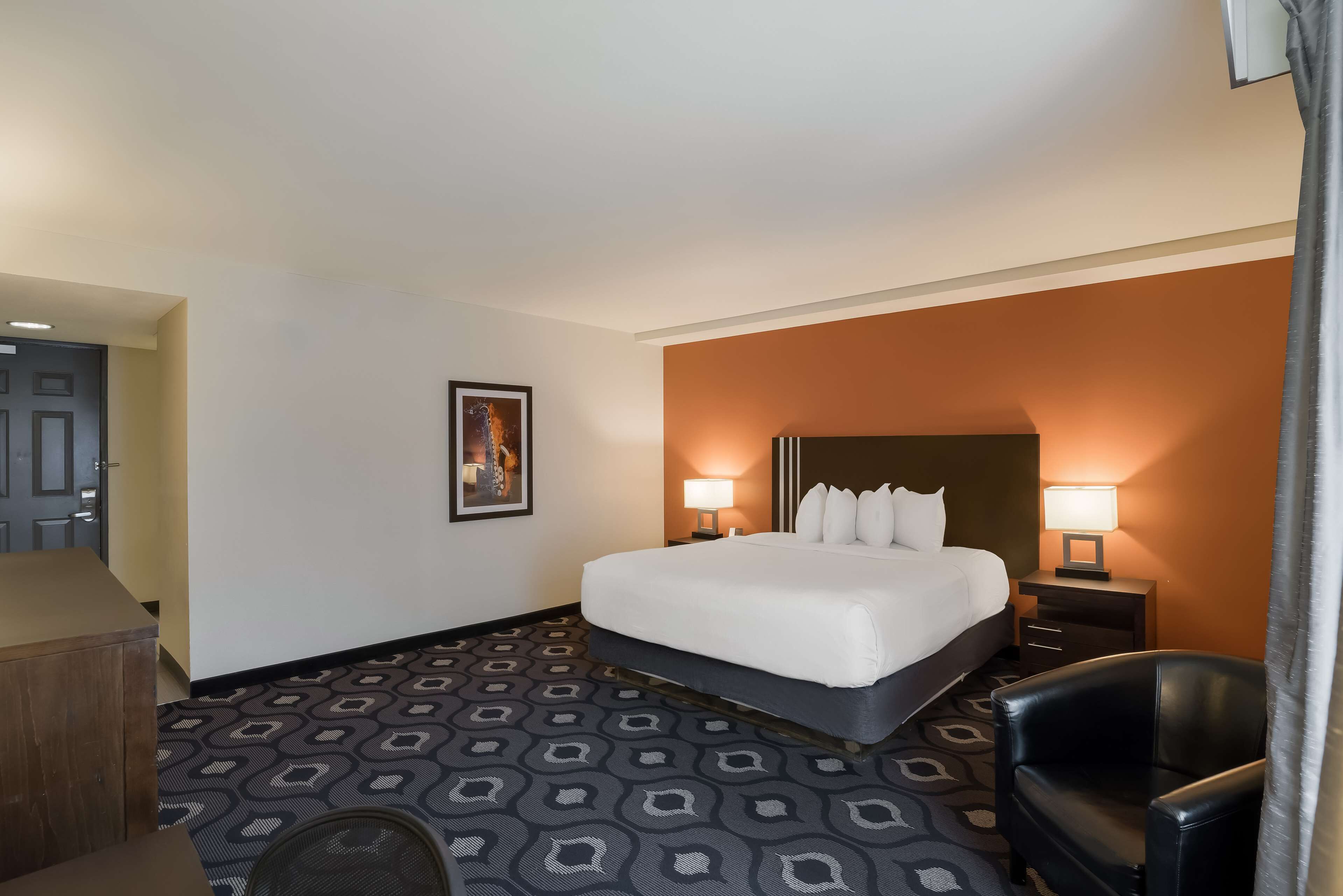 A hotel room with a large bed, two bedside lamps, a chair, and a patterned carpet.