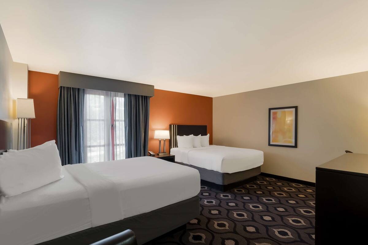 A hotel room with two beds, a desk, a lamp, a window with curtains, and a patterned carpet.