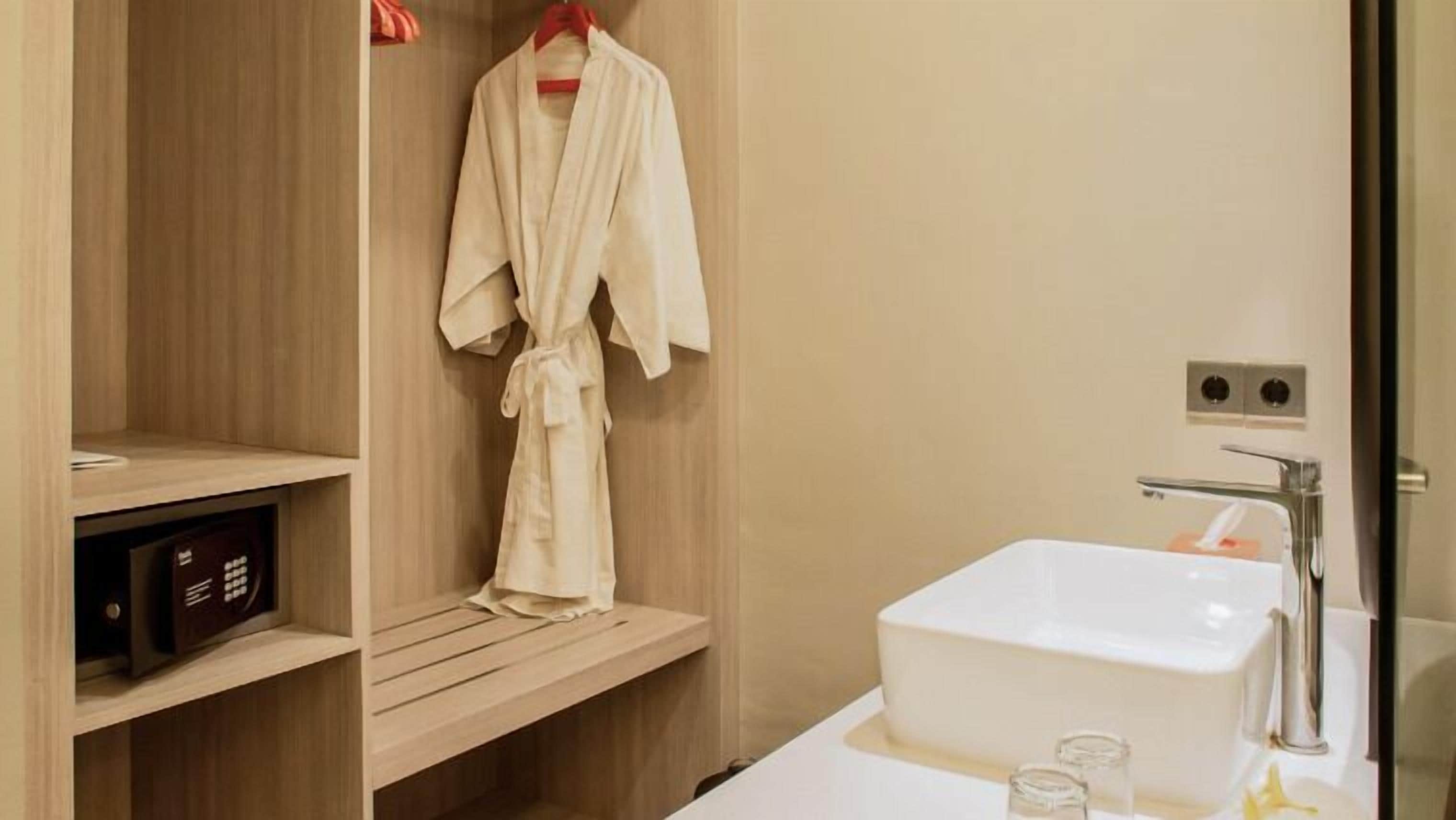 A modern bathroom with a wooden vanity, a white sink, and a robe hanging on a rack.