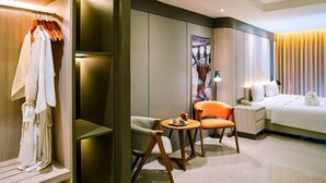 Een moderne hotelkamer met een bed, een zithoek met twee stoelen, een kleine tafel en een kledingkast.