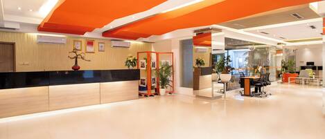 A modern hotel lobby with a reception desk, seating area, and potted plants.