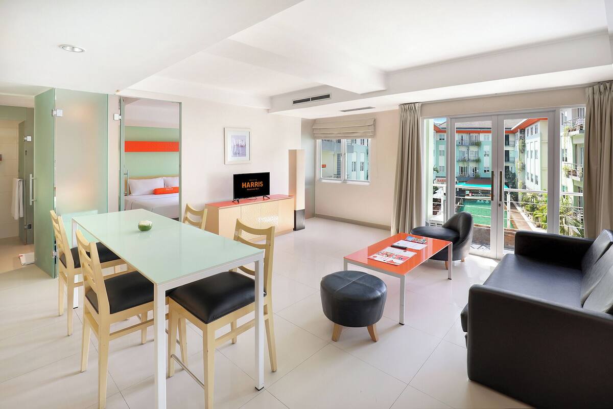 Ein modernes Hotelzimmer mit Essbereich, einer Couch, einem Fernseher und einem Balkon mit Blick auf Gebäude.