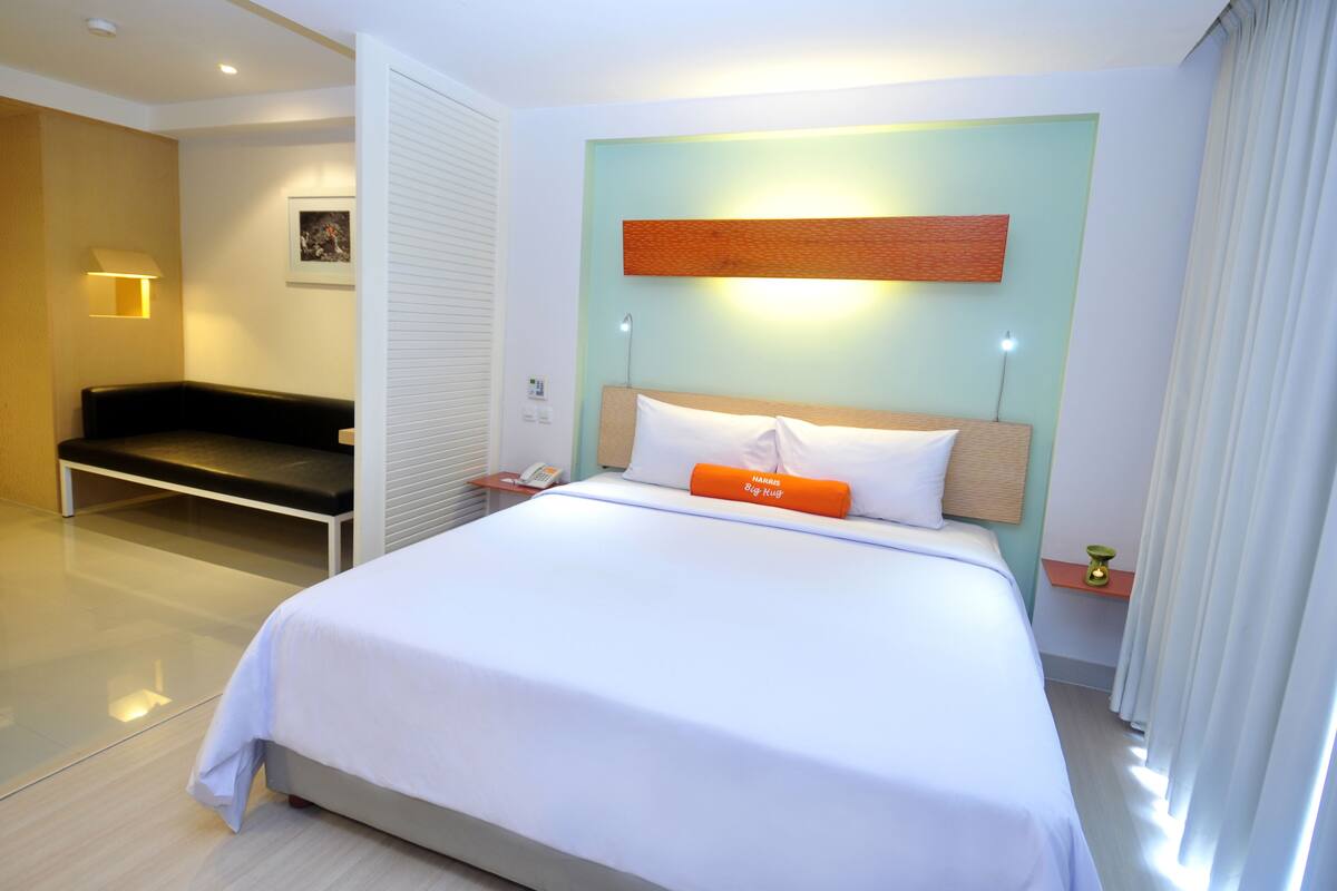 Ein modernes Hotelzimmer mit einem großen Bett, einer Bank, einem Nachttisch und einer wandmontierten Leuchte.