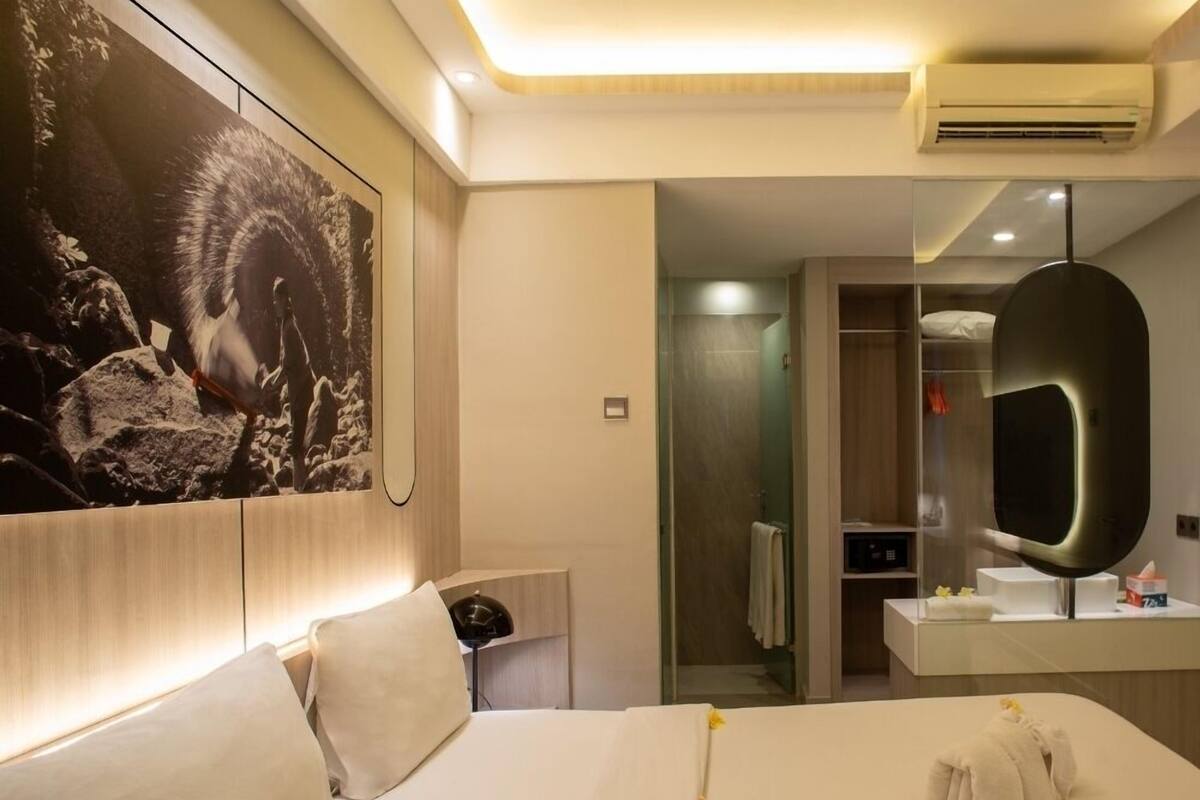 Ein Hotelzimmer mit einem großen Bett, einem Nachttisch, einem Spiegel und einem an der Wand hängenden Kunstwerk.