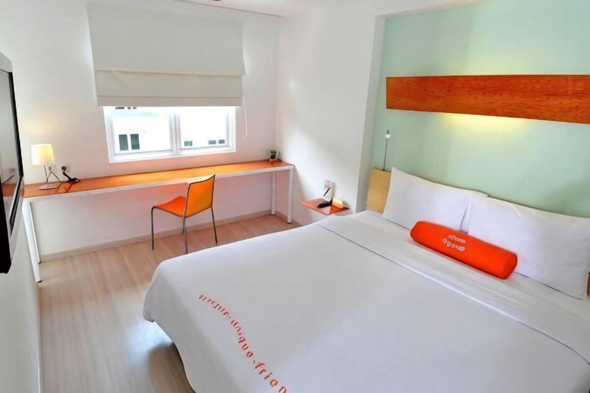 Ein Hotelzimmer mit Bett, Schreibtisch, Stuhl, Fenster und Nachttisch.