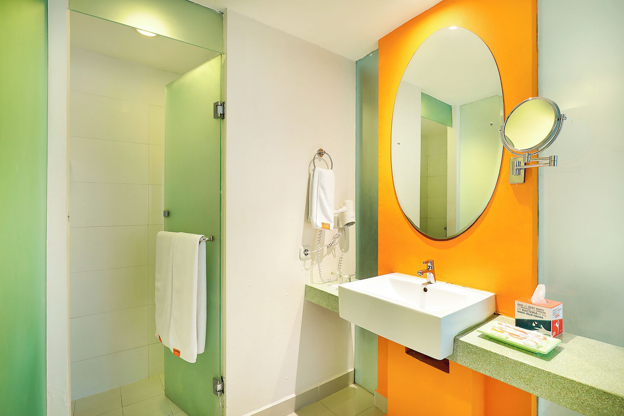 A bathroom with a green and orange color scheme, a white sink, a mirror, and a towel hanging on the wall.