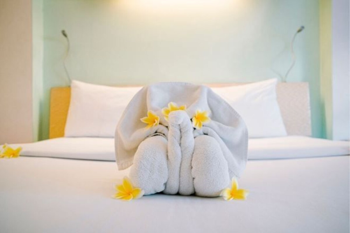 Ein Bett mit einem in Menschengestalt gefalteten Handtuch, Kissen und einer wandmontierten Lampe.
