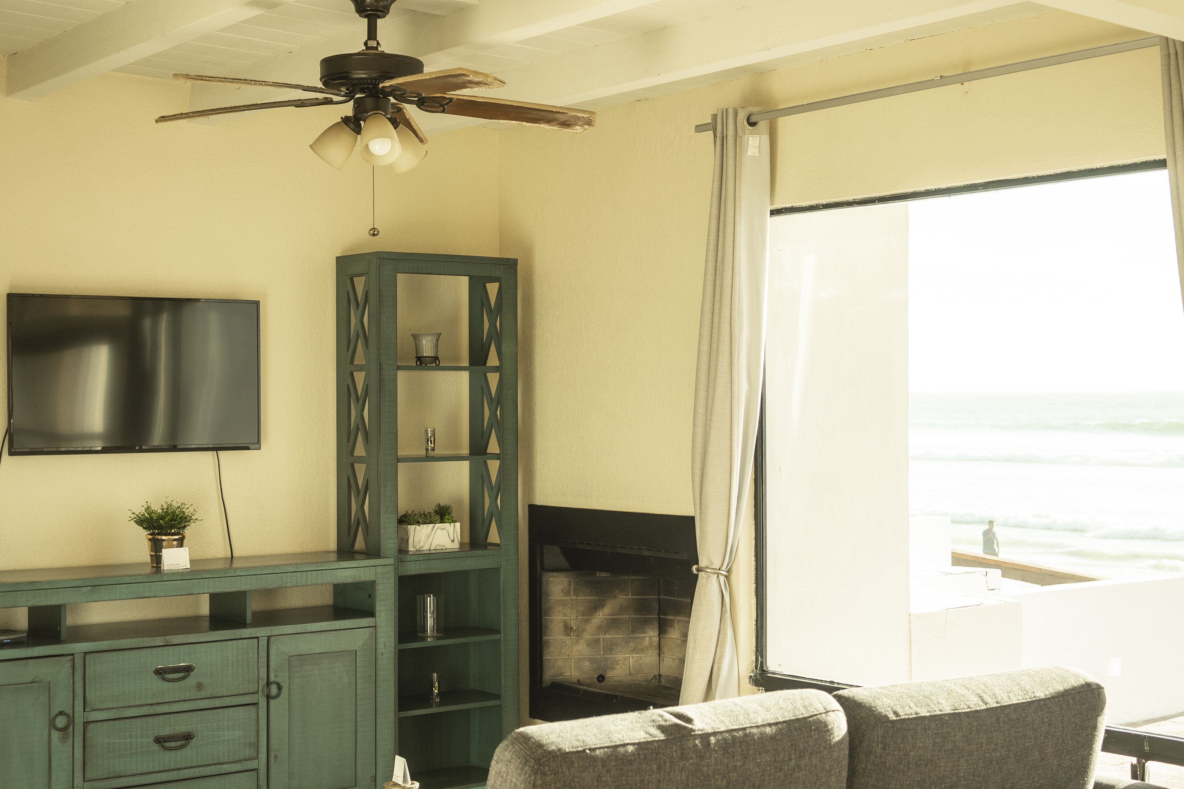 A living room with a TV, a fireplace, a ceiling fan, and a view of the ocean.