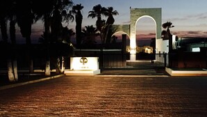 Un área de acceso pavimentada con un llamativo letrero iluminado y una cerca.