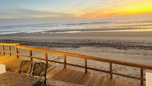 Una terraza de madera con barandilla que da a una playa al atardecer.