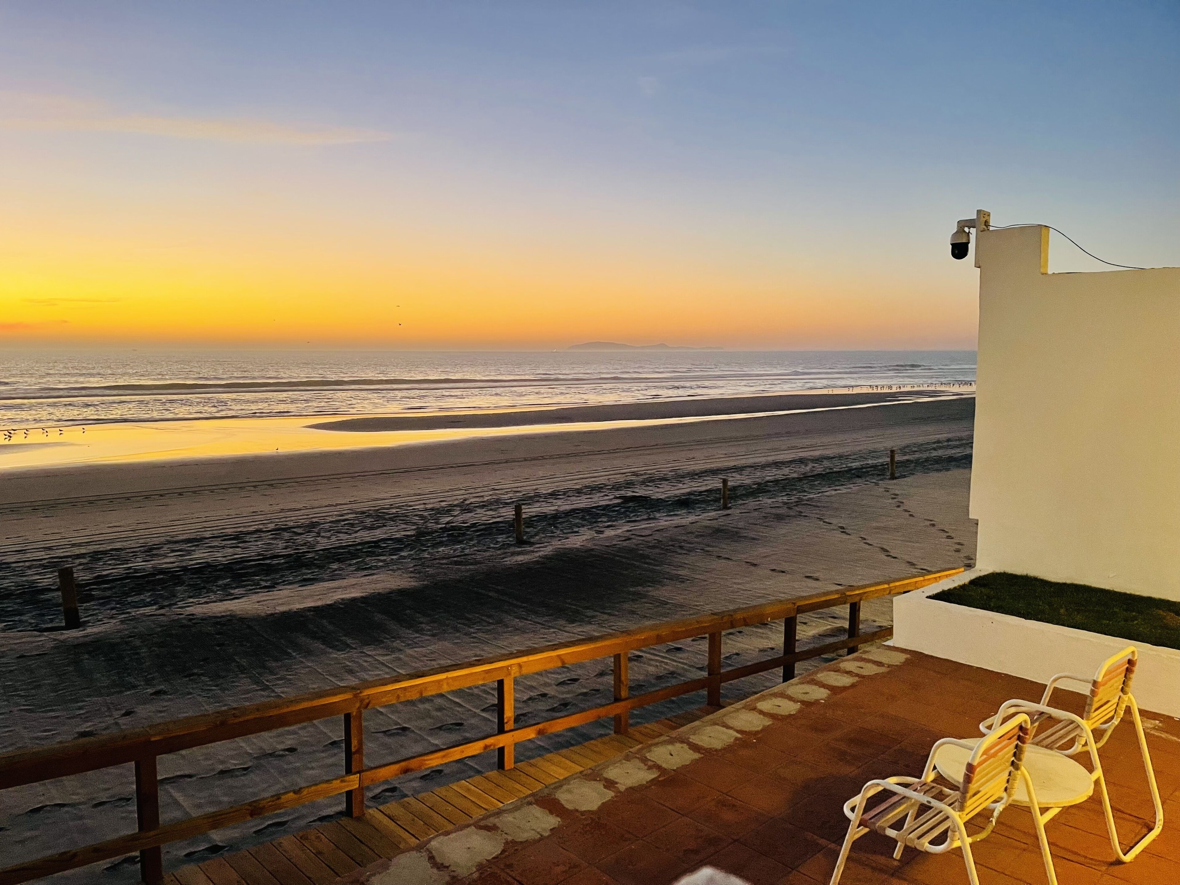 A balcony with a view of the beach and ocean at sunset.