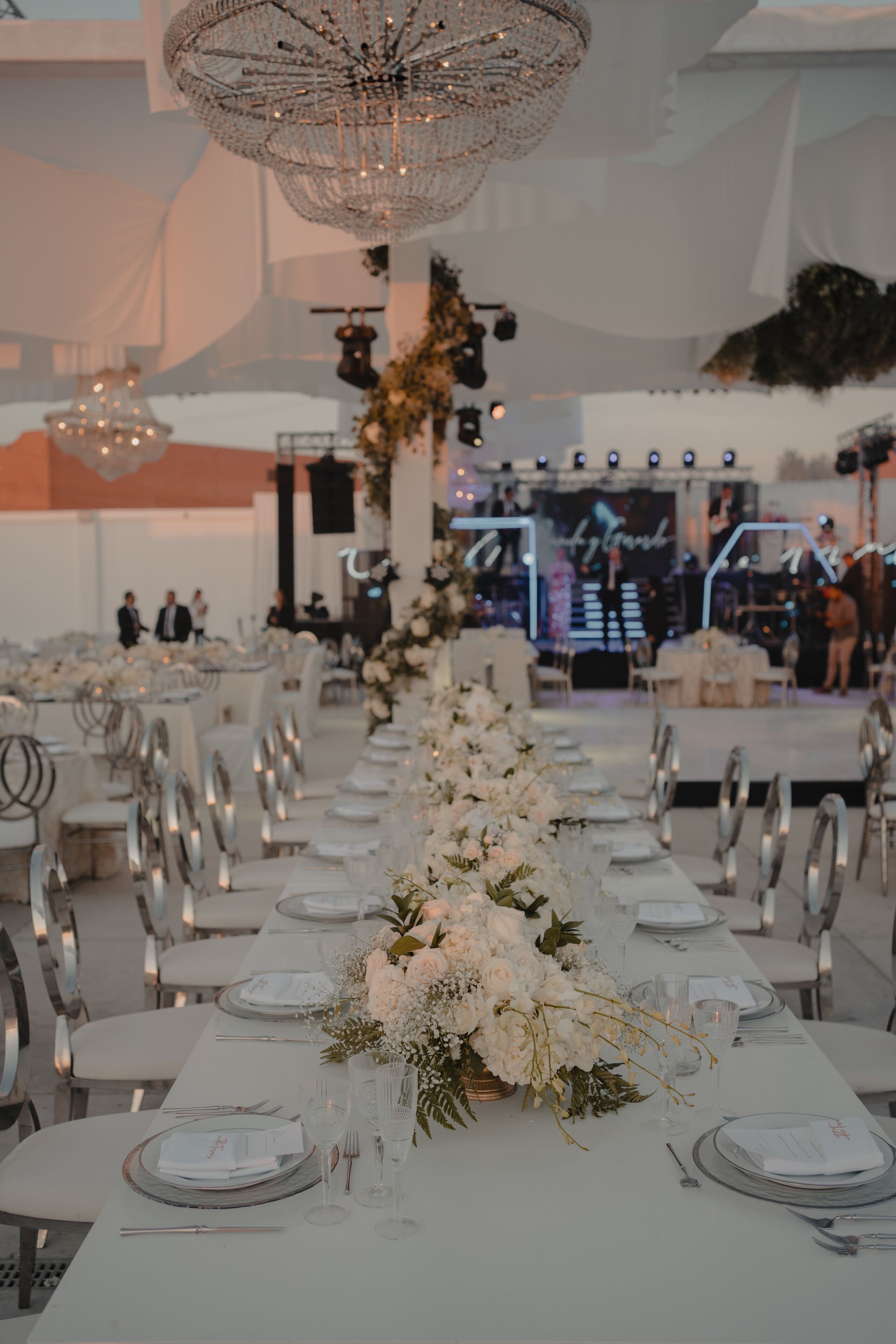 Una larga mesa de banquete con manteles blancos, cubiertos y cristalería, preparada para un evento formal.