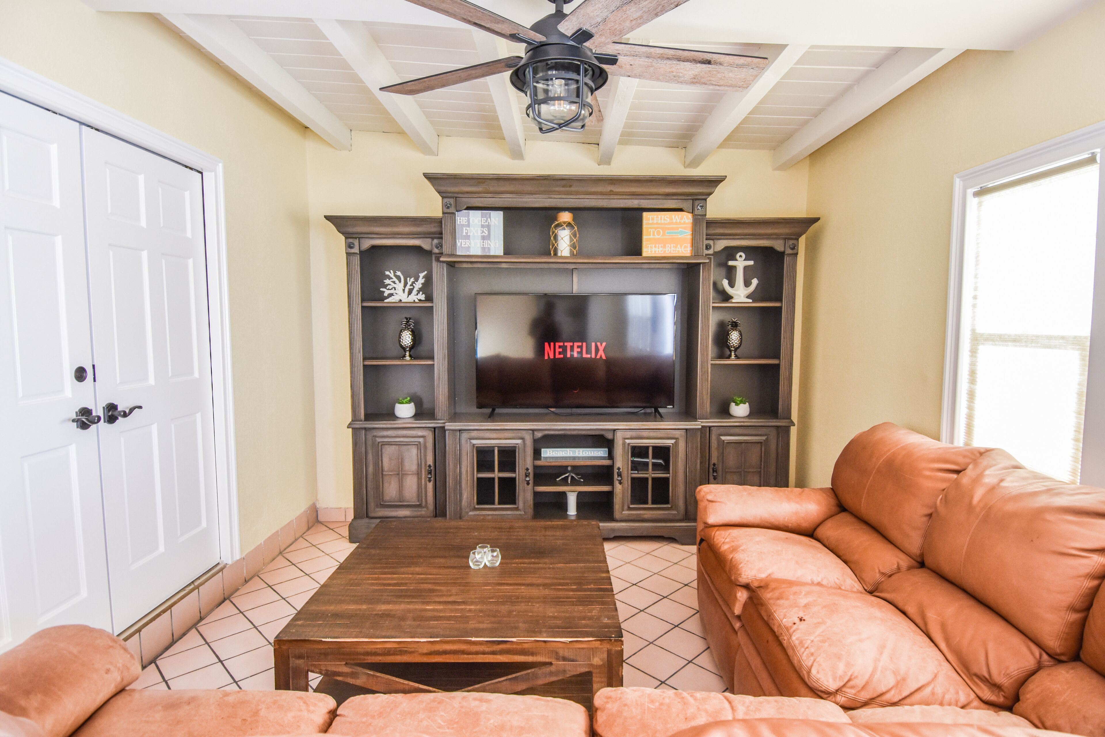 A living room with a television, wooden cabinets, a ceiling fan, and a sofa.
